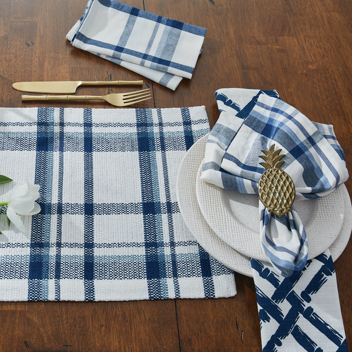 Table setting on a dark wood table with a blue and white plaid placemat, with napkins. 